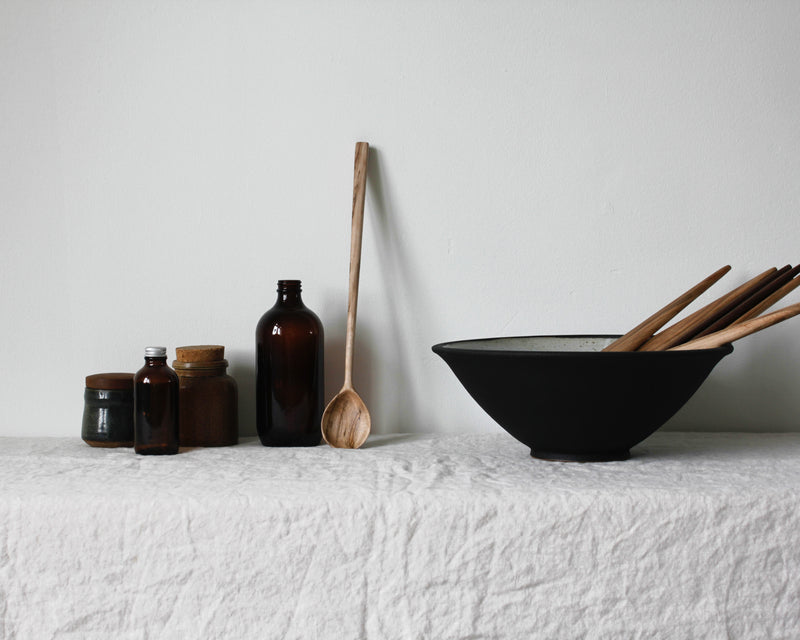 Wooden string spoon on table next to black bowl with wooden salad servers