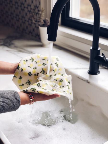 hands holding lemon swedish sponge cloth over sink with water running