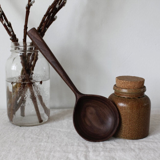 woodsmans daughter walnut round serving spoon leaning on table next to ceramic container