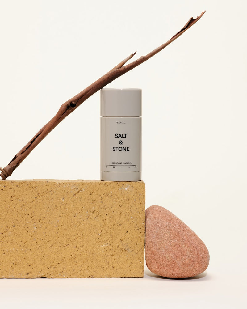 salt and stone santal natural deodorant on wood block with peach rock on side and stick above