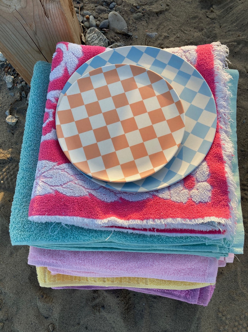 bamboo side and dinner checkers plates stacked on towels on the beach