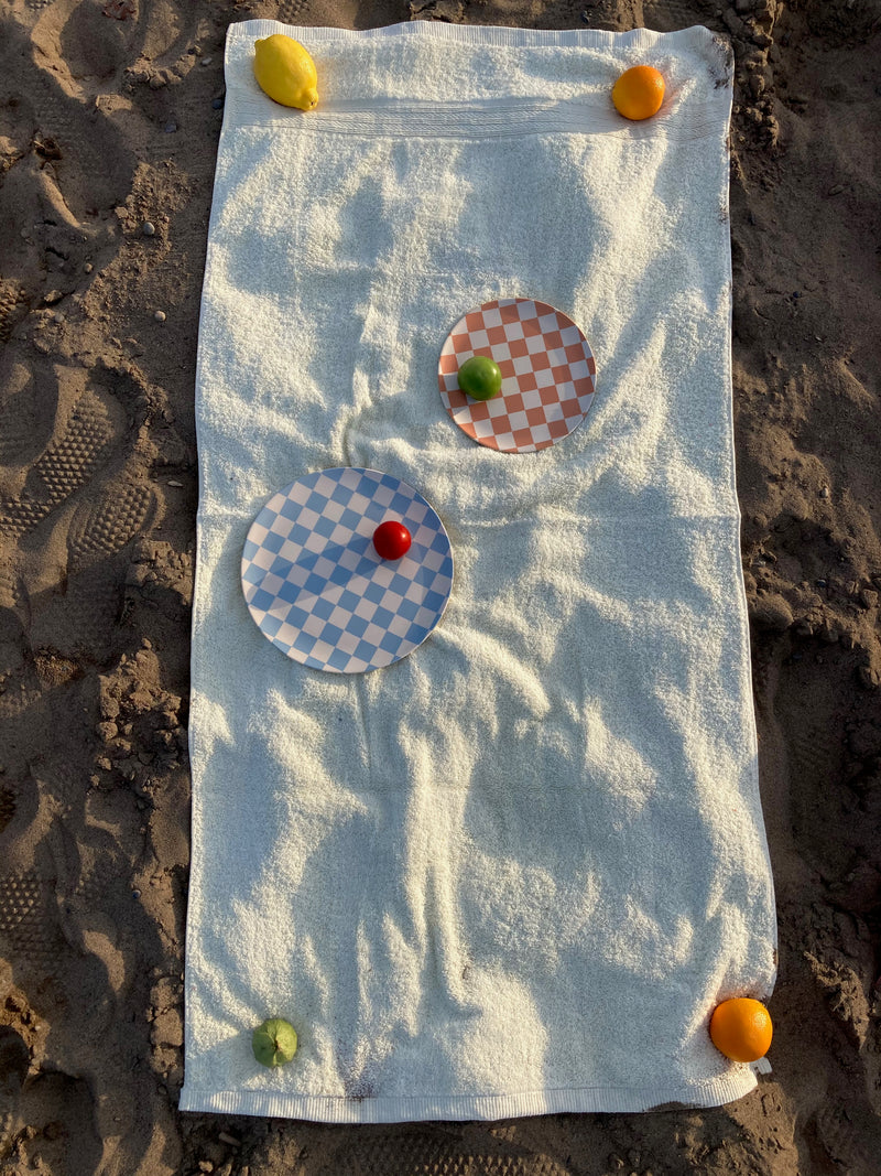 bamboo side and dinner plates in blue and peach checkers on a towel at the beach