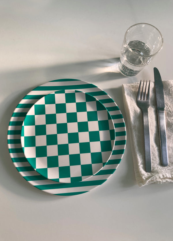 bamboo side and dinner plate in green stripes and green checkers stacked on table with napkin fork and knife