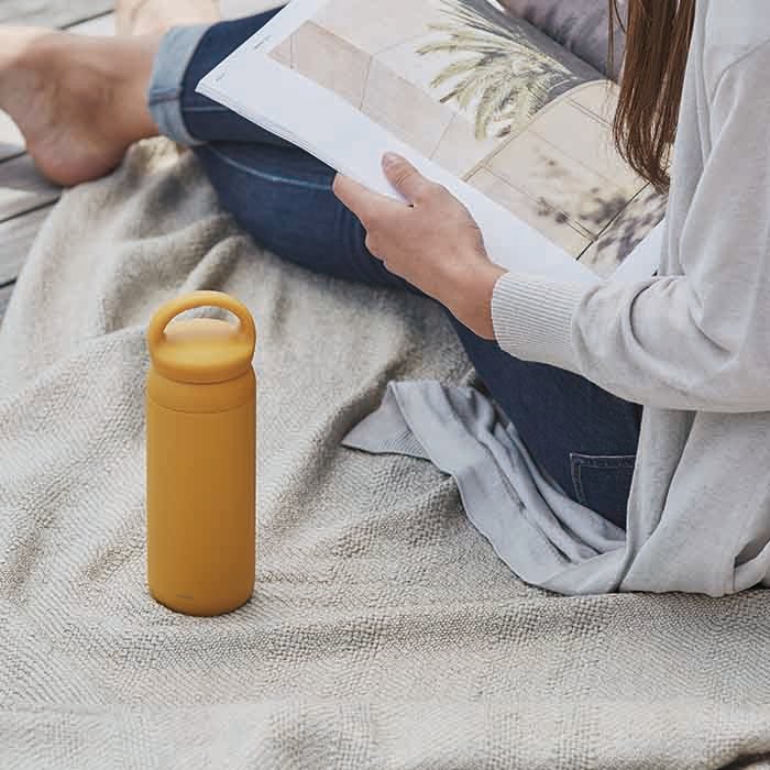 kinto mustard day off tumbler upright on blanket with girl sitting next to it