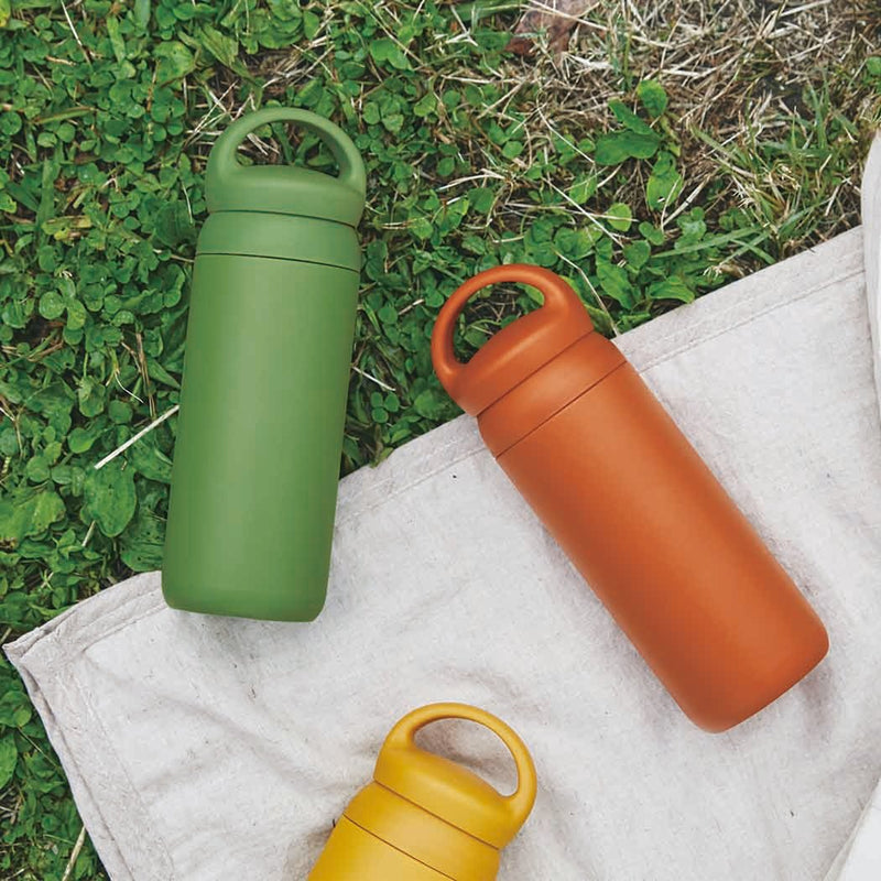 kinto vacuum insulated water bottles orange yellow and green laying on blanket and grass