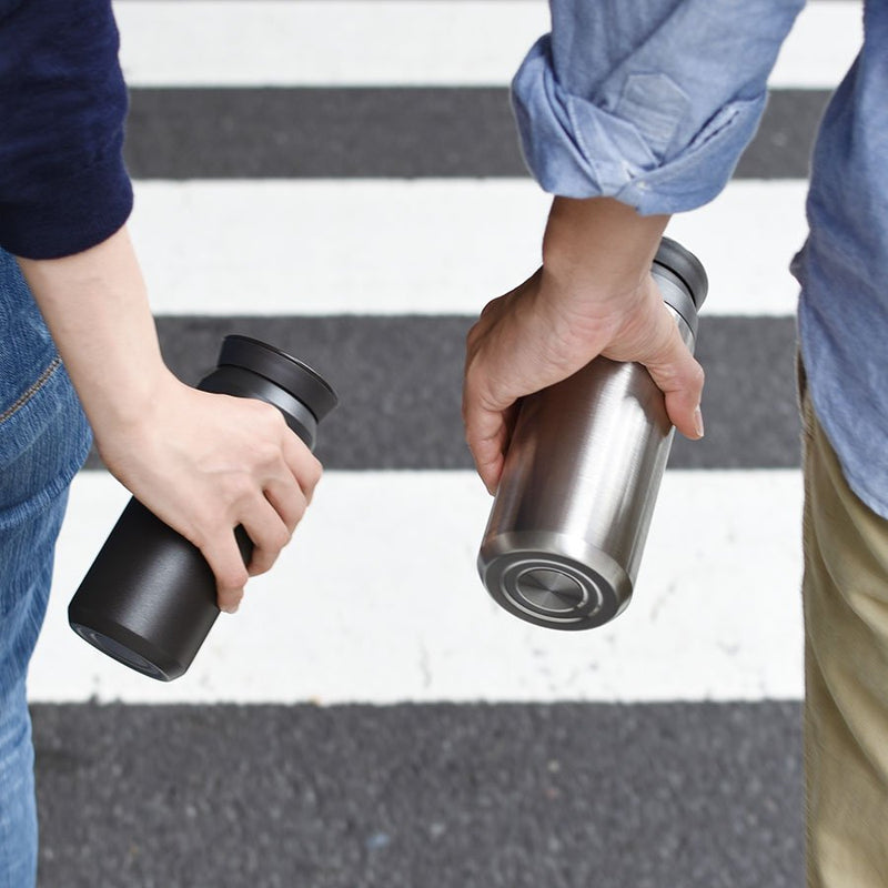 two people walking holding black and silver travel tumbler