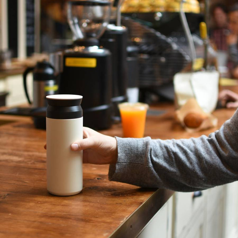 hand holding white kinto travel tumbler on coffee counter