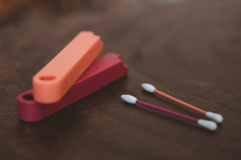 Red and peach reusable cotton swabs for make up side by side next to their biodegradable cases
