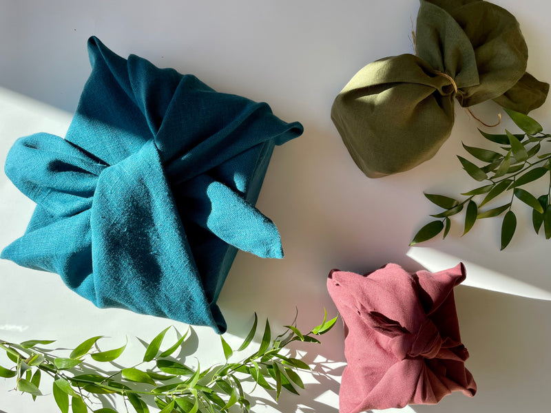 three boxes wrapped in furoshiki wraps in different sizes and colours -  marine, moss and plum