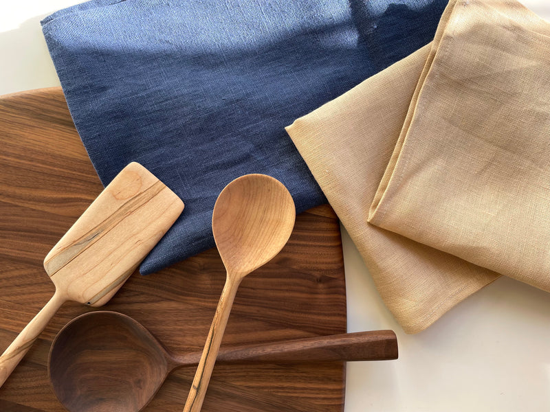 linen tea towel and napkins layer on walnut cutting board with wooden spoons