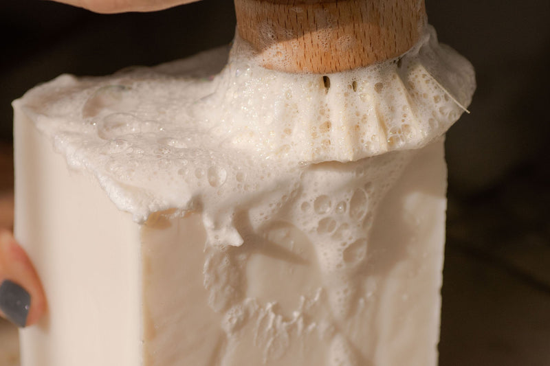 bamboo dish brush being rubbed on solid dish soap block causing a lather
