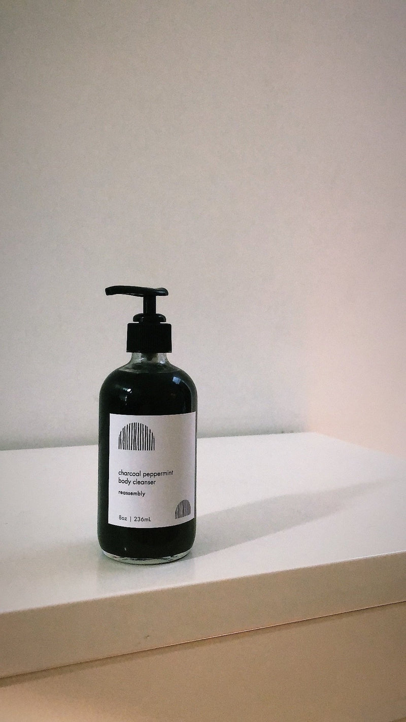 reassembly botanical charcoal peppermint body cleanser in glass pump bottle on white counter top