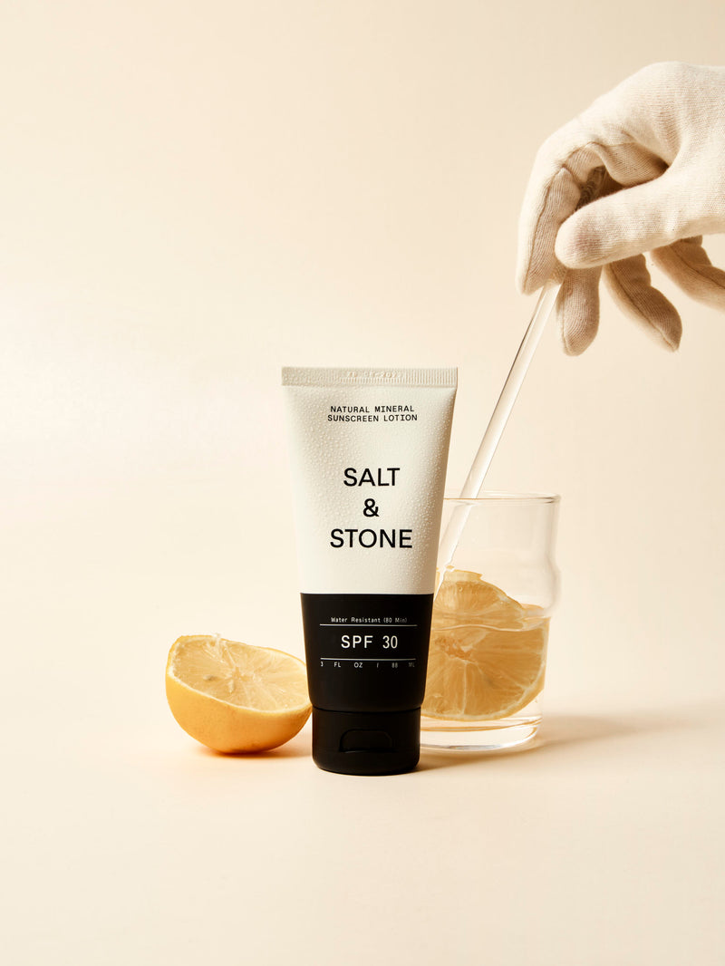 salt and stone spf 30 sunscreen lotion next to glass of lemon water being stirred