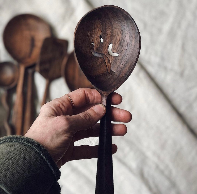 walnut wood slotted spoon being held by woman hand