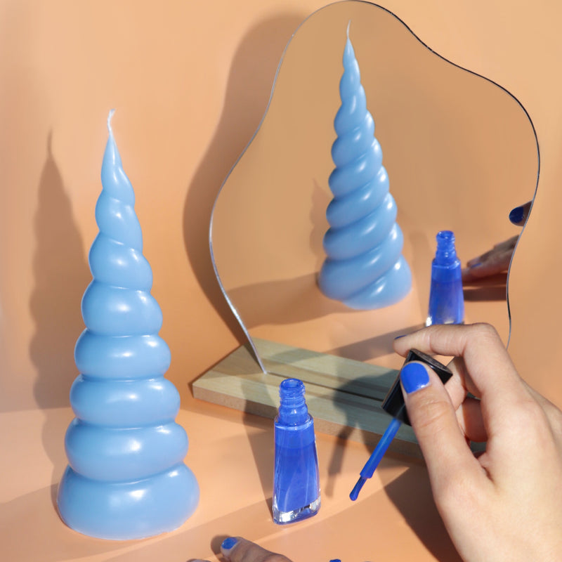 mann blue swirl candle on peach counter with mirror reflecting candle and girl painting nails blue