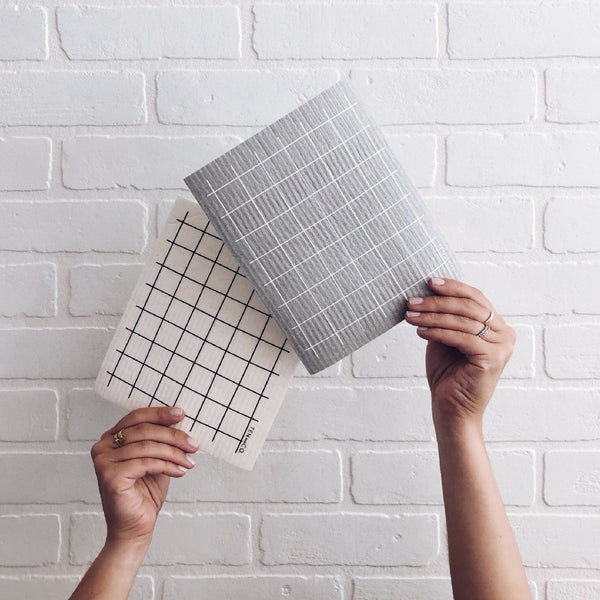 hands hold up Swedish sponge cloths in grey grid and white grid pattern