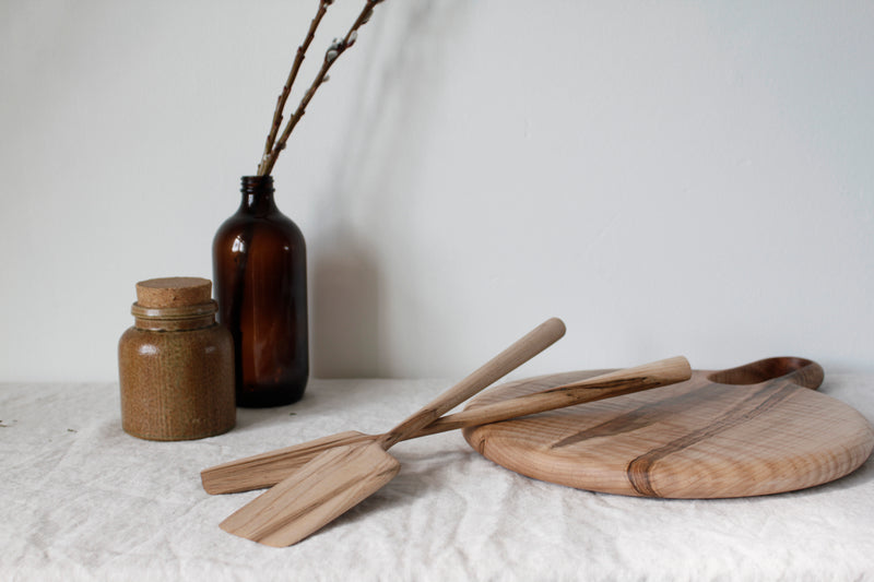 the woodsmans daughter handmade maple and walnut spatulas laying across table round cheese board