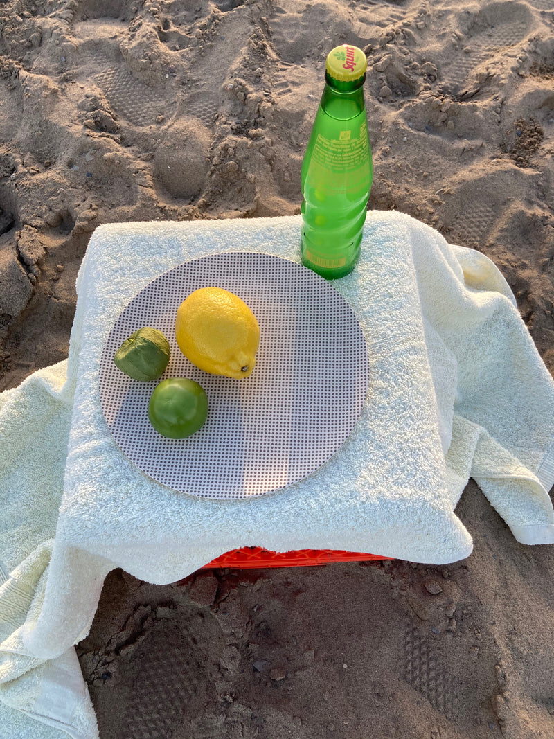towel on sand with dinner popdot xenia taler bamboo plate on top with lemon on limes
